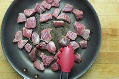 meat being cooked in a frying pan with tongs on a wooden counter top