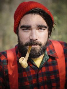 a bearded man with a pipe in his mouth wearing an orange vest and red hat