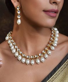 Be the divine bliss of beauty with this Gold Toned White Handcrafted Brass Kundan Necklace with Earrings Set. It is an intricately handcrafted brass Kundan necklace with pearl detailing that comes with a pair of matching earrings. Pearl Kundan Necklace For Gift, Elegant Brass Jewelry Sets For Festivals, Kundan Necklace With Pearl Chain For Celebration, Pearl Chain Jewelry Sets For Celebration, Pearl Drop Necklace For Celebrations, Celebration Pearl Necklace For Diwali, Pearl Drop Jewelry For Festivals, Elegant Chandbali Bridal Necklace In Brass, Pearl Temple Jewelry