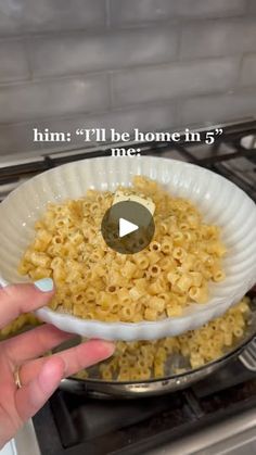 a person holding a bowl of macaroni and cheese in front of an oven