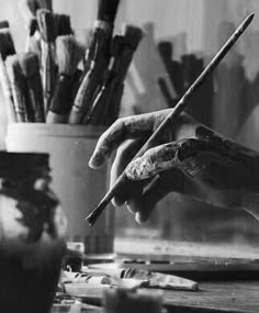 a black and white photo of someone's hand holding a paintbrush in front of some brushes