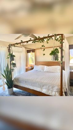 a bed with white sheets and pillows in a bedroom next to a potted plant