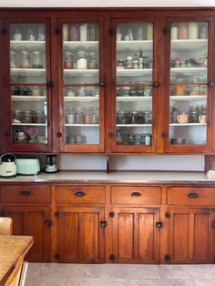 a wooden cabinet with glass doors and shelves in the middle of an empty dining room