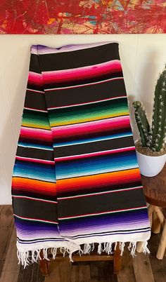 a colorful blanket sitting on top of a wooden table next to a potted cactus