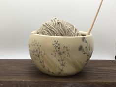 a ball of yarn in a bowl on top of a wooden table next to a crochet hook