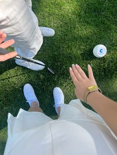 two people standing in the grass with their hands on each other's legs and one person holding out her hand