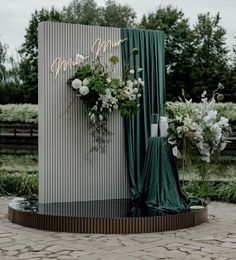 an outdoor ceremony setup with flowers and greenery on the side, surrounded by green drapes