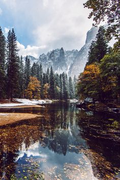 a lake surrounded by trees and snow covered mountains in the background, with water running through it