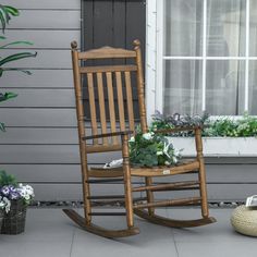 a wooden rocking chair sitting on top of a patio next to a potted plant