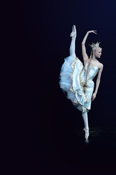 the ballerina is dressed in white and gold with her arms stretched out while she balances on one leg