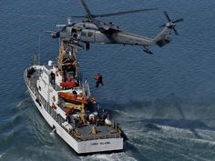 a helicopter is flying over a boat in the water with it's landing gear down