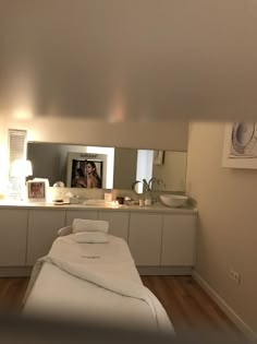 a white bed sitting in a bedroom next to a bathroom sink under a large mirror