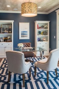 a dining room with blue walls and white trim on the ceiling, two chairs are in front of a glass table