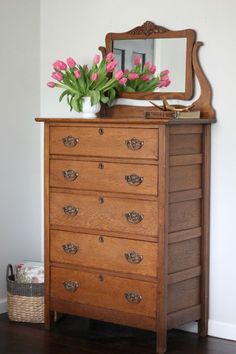 a wooden dresser with pink flowers on top and a mirror above it in a bedroom