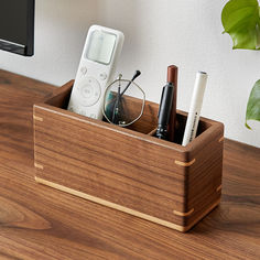 a wooden box with pens, eyeglasses and an electronic device in it sitting on a desk