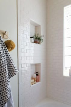 a white tiled bathroom with black and white towels hanging on the shower wall next to a bathtub