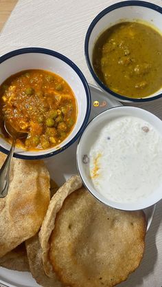 three bowls of soup and two pita breads on a plate