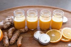 several mason jars filled with orange juice next to sliced lemons and ginger