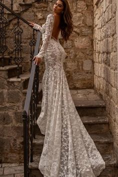 a woman in a long sleeved wedding dress is standing on stairs with her back to the camera