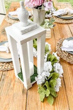 a wooden table topped with white vases filled with pink and green flowers next to plates