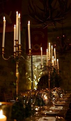 a long table with candles and place settings on it in a dimly lit dining room