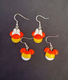 three pairs of mickey mouse earring and pendants on a black surface with white, orange and yellow beads