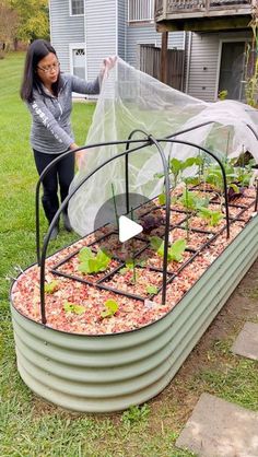 a woman standing next to a garden bed with plants in it and a plastic cover over the top