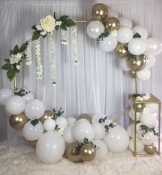 white and gold balloons are arranged in the shape of an arch with greenery on it