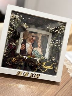 a wedding photo frame with flowers and the couple's name is displayed on a table