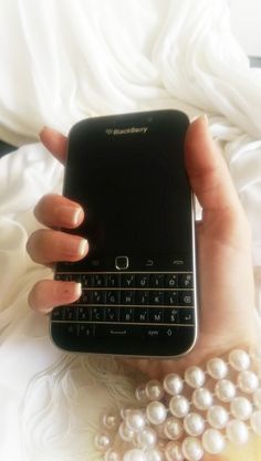 a person holding a cell phone in their hand with pearls on the table next to it