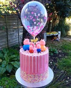 a pink cake with peppa pig figures on top and a large balloon in the air