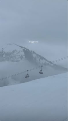 a ski lift going up the side of a mountain covered in snow with fog on it