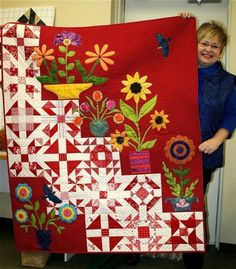 a woman holding up a red quilt with flowers on it