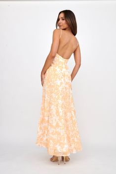 the back of a woman in an orange and white floral print dress, with her hands on her hips