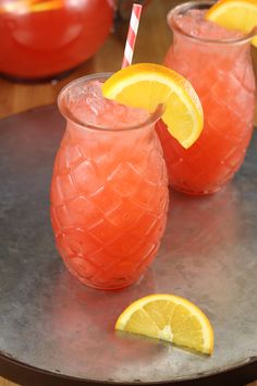 two glasses filled with watermelon lemonade on top of a metal tray next to orange slices