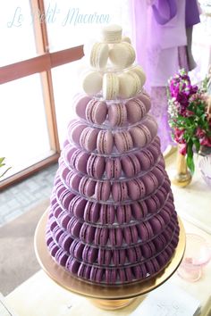 a purple and white cake with macaroons stacked on it's sides in front of a window