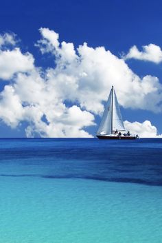 a sailboat floating in the ocean on a sunny day with blue sky and clouds