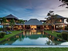 a large pool in the middle of a lush green yard next to two houses with thatched roofs