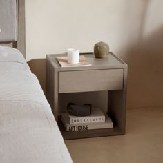 a nightstand with two books and a cup on it next to a white bedspread