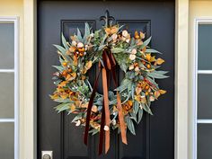 a wreath on the front door of a house with orange and green flowers hanging from it