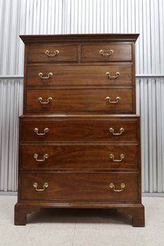 an old wooden dresser with brass handles in front of a corrugated wall and white tile floor