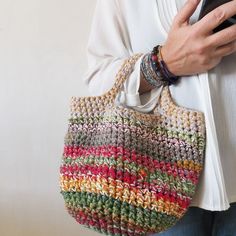 a woman is holding a crocheted purse and looking at her cell phone while wearing a white shirt