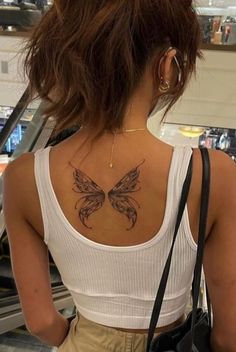 a woman with a butterfly tattoo on her back is looking at an escalator