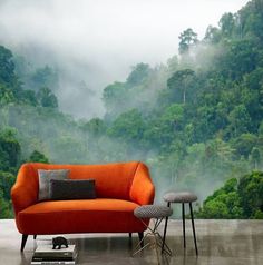 an orange couch and two stools in front of a forest scene wallpaper mural