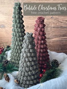 three crocheted christmas trees sitting on top of a white cloth next to pine cones