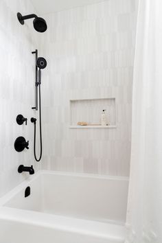 a white bathroom with a black shower head and hand held shower faucet next to the bathtub