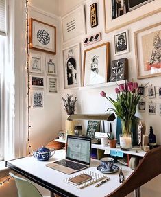 a laptop computer sitting on top of a white desk in front of a bunch of framed pictures