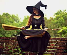 a woman dressed as a witch sitting on a brick wall