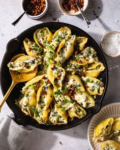 a skillet filled with shells covered in spinach and cheese, next to bowls of other ingredients