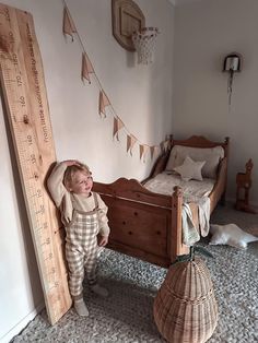 a little boy standing next to a bed in a room with a large wooden ruler on the wall